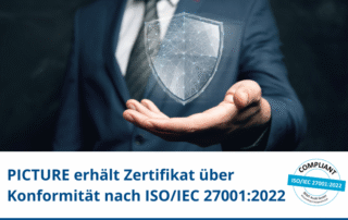 Mann im Anzug hält stilisiertes digitales Schild. Text: „PICTURE erhält Zertifikat über Konformität nach ISO/IEC 27001:2022“. Prüfsiegel mit Aufschrift „COMPLIANT“ unten rechts sichtbar.