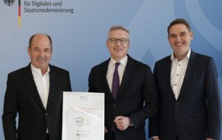 Drei Männer im Anzug vor Logo des Bundesministeriums für Digitales und Staatsmodernisierung, einer hält Urkunde „Software Made in Germany“.